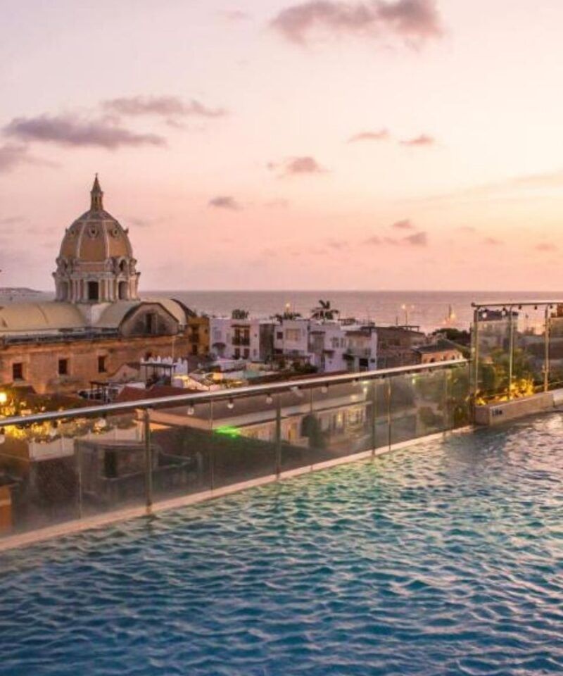 Piscina infinita con vista al atardecer de Cartagena y la torre de San Pedro Claver, lujo caribeño y elegancia histórica.