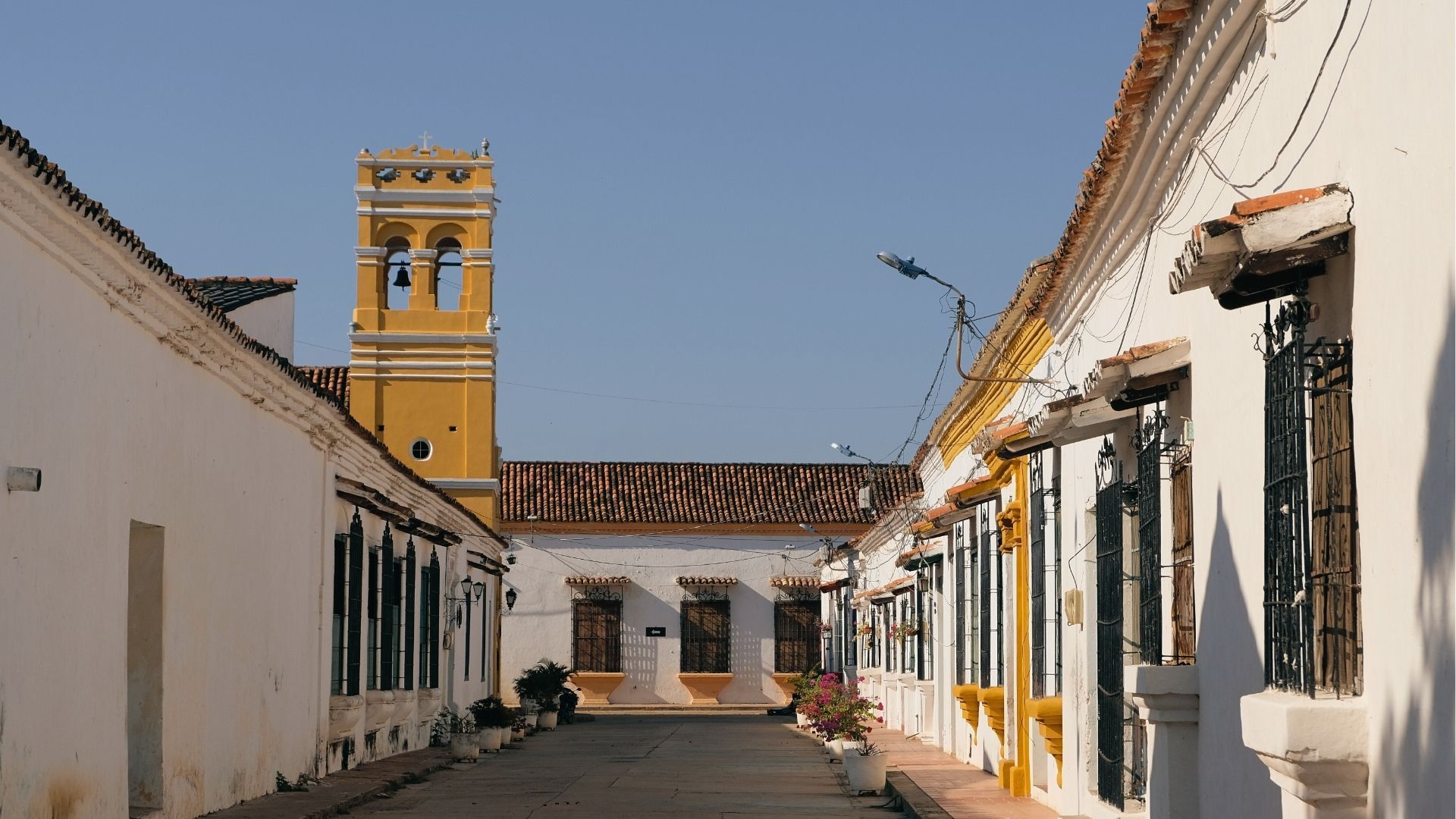 Calles de Mompox al atardecer, torre amarilla iluminada bajo cielo azul caribeño.